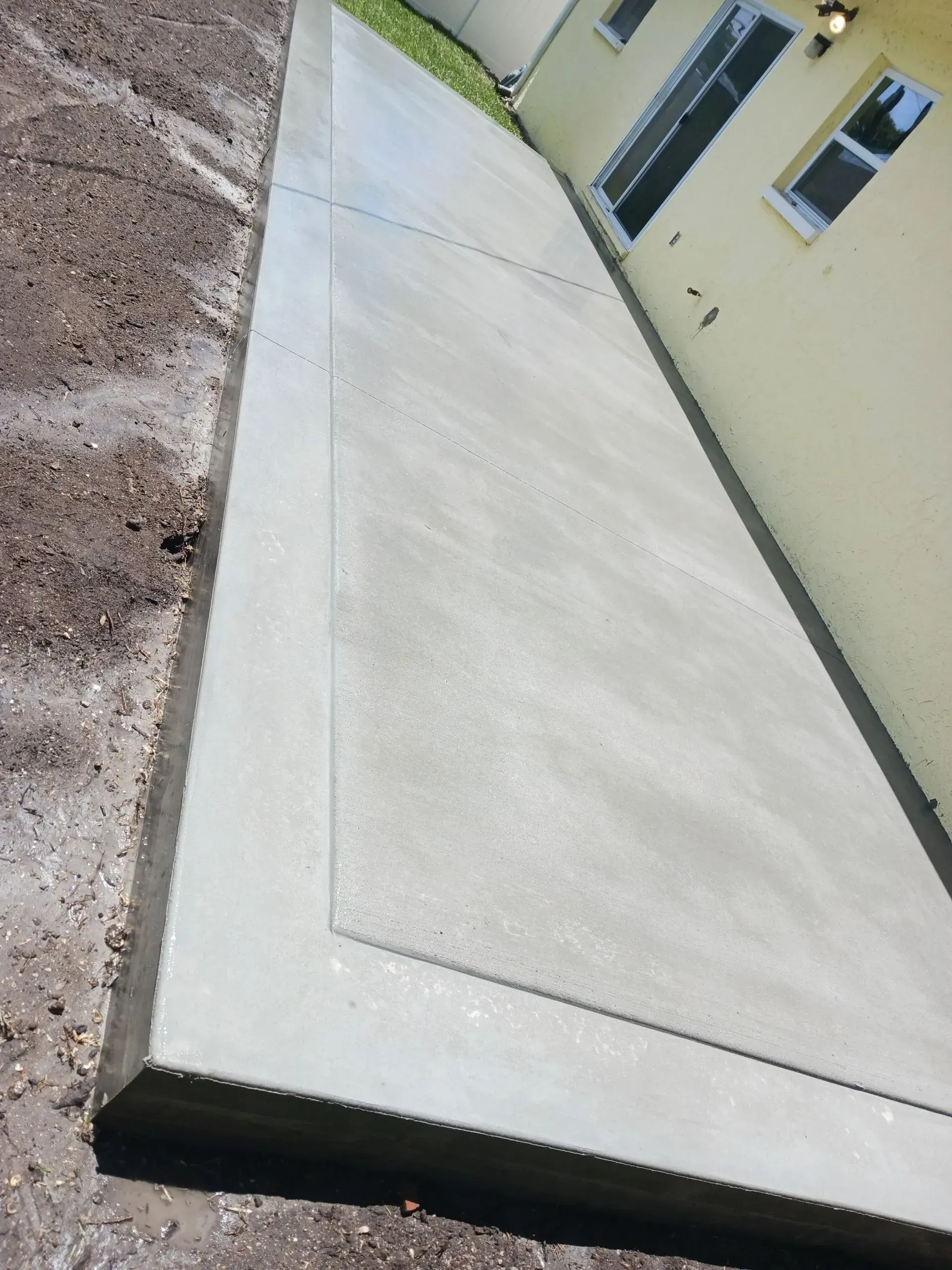 Tilted view of a concrete sidewalk beside a beige building and dirt ground