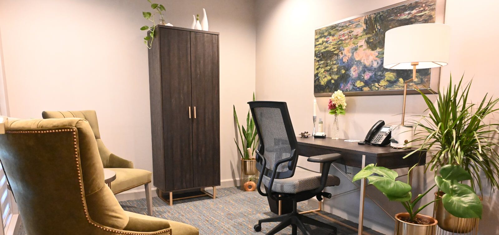 A room with a desk , chair , couch and plants.
