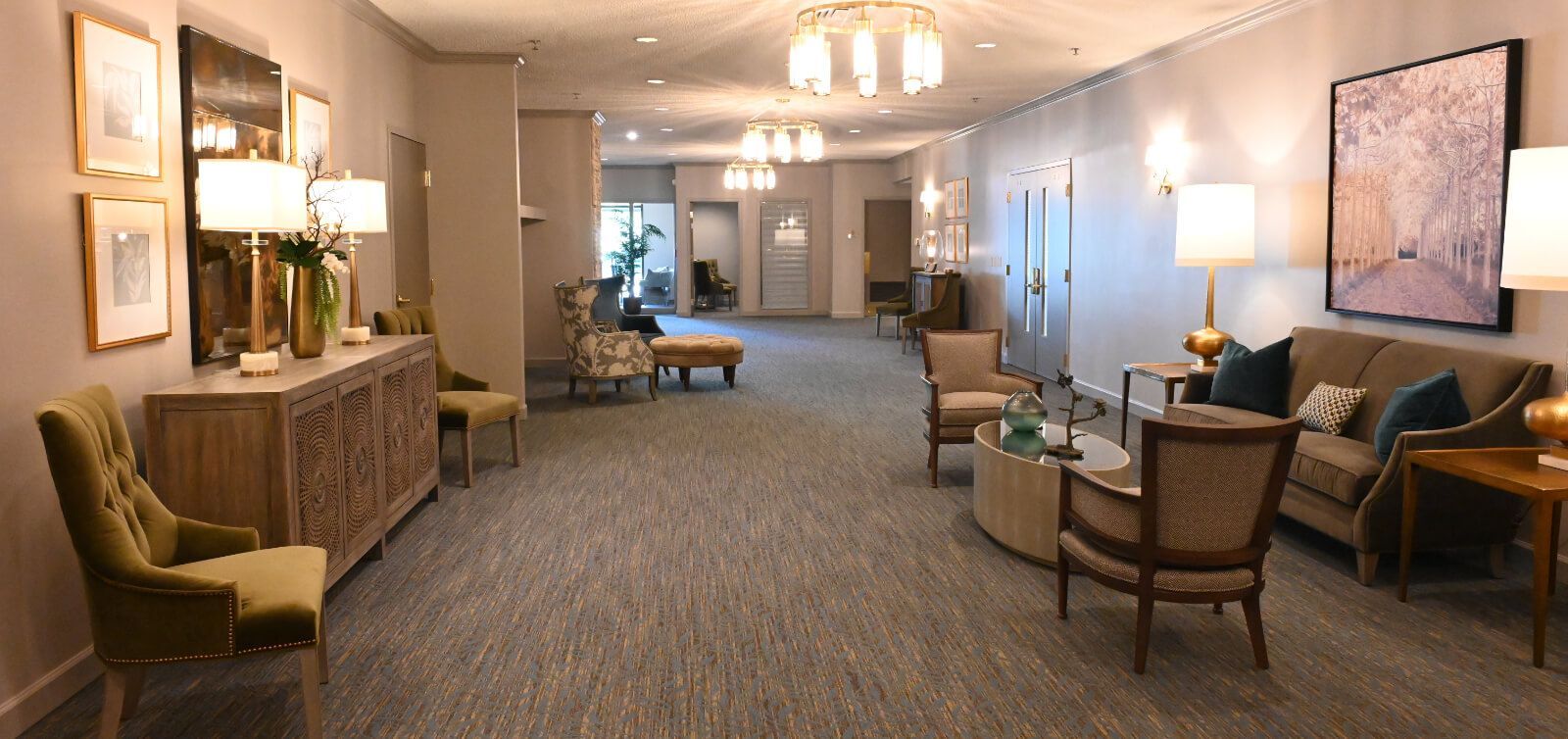 A long hallway with a couch , chairs , tables and lamps.