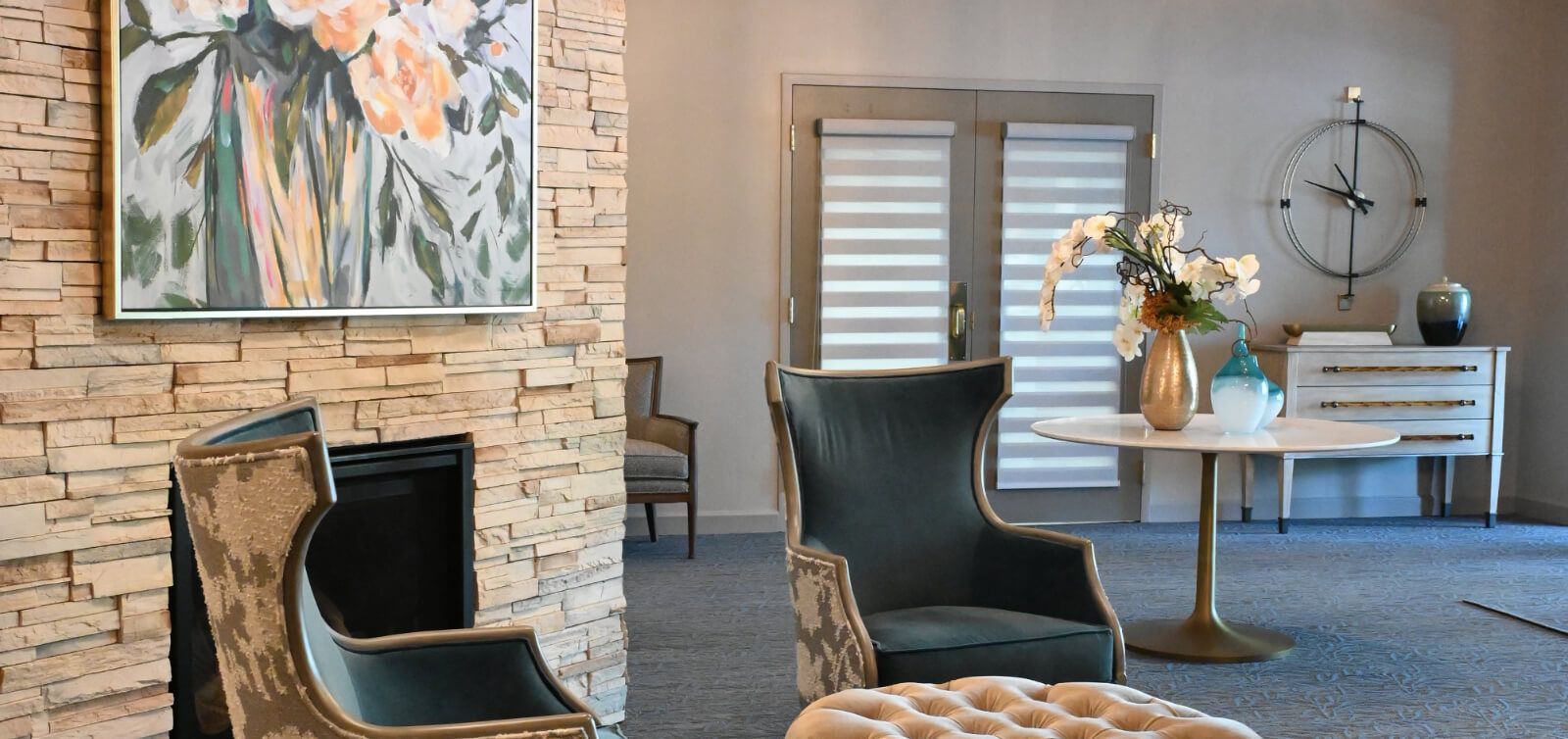 A living room with chairs , a table , a fireplace and a clock on the wall.