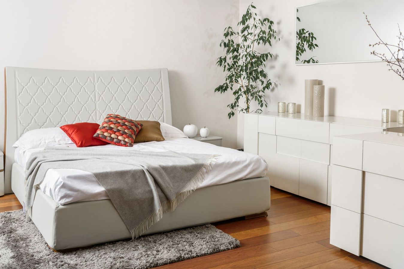 Camera da letto moderna con letto, tavolino, pavimenti scuri e specchi decorativi.
