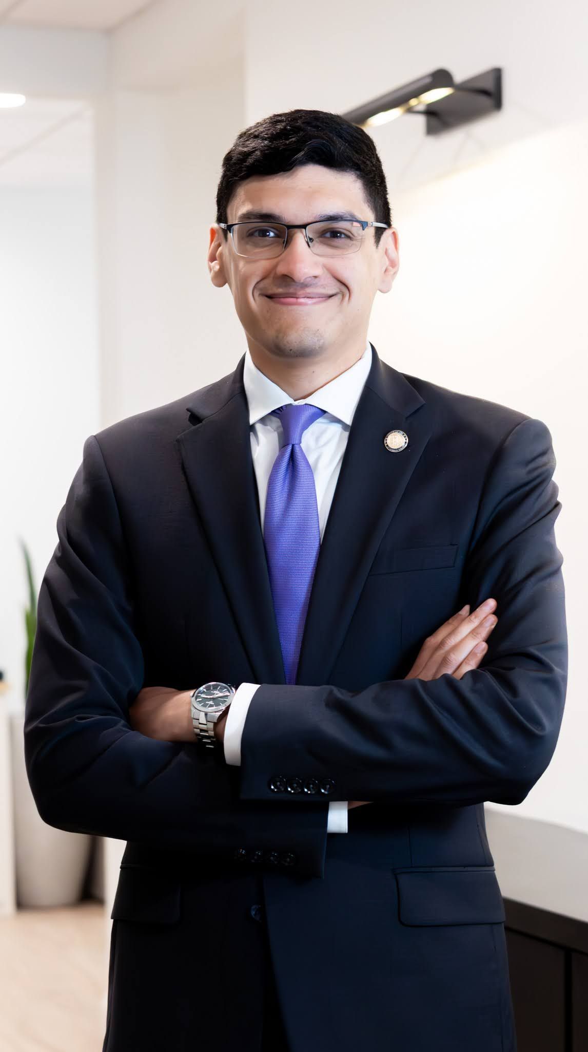 A man in a blue suit and tie is standing in front of a white wall.