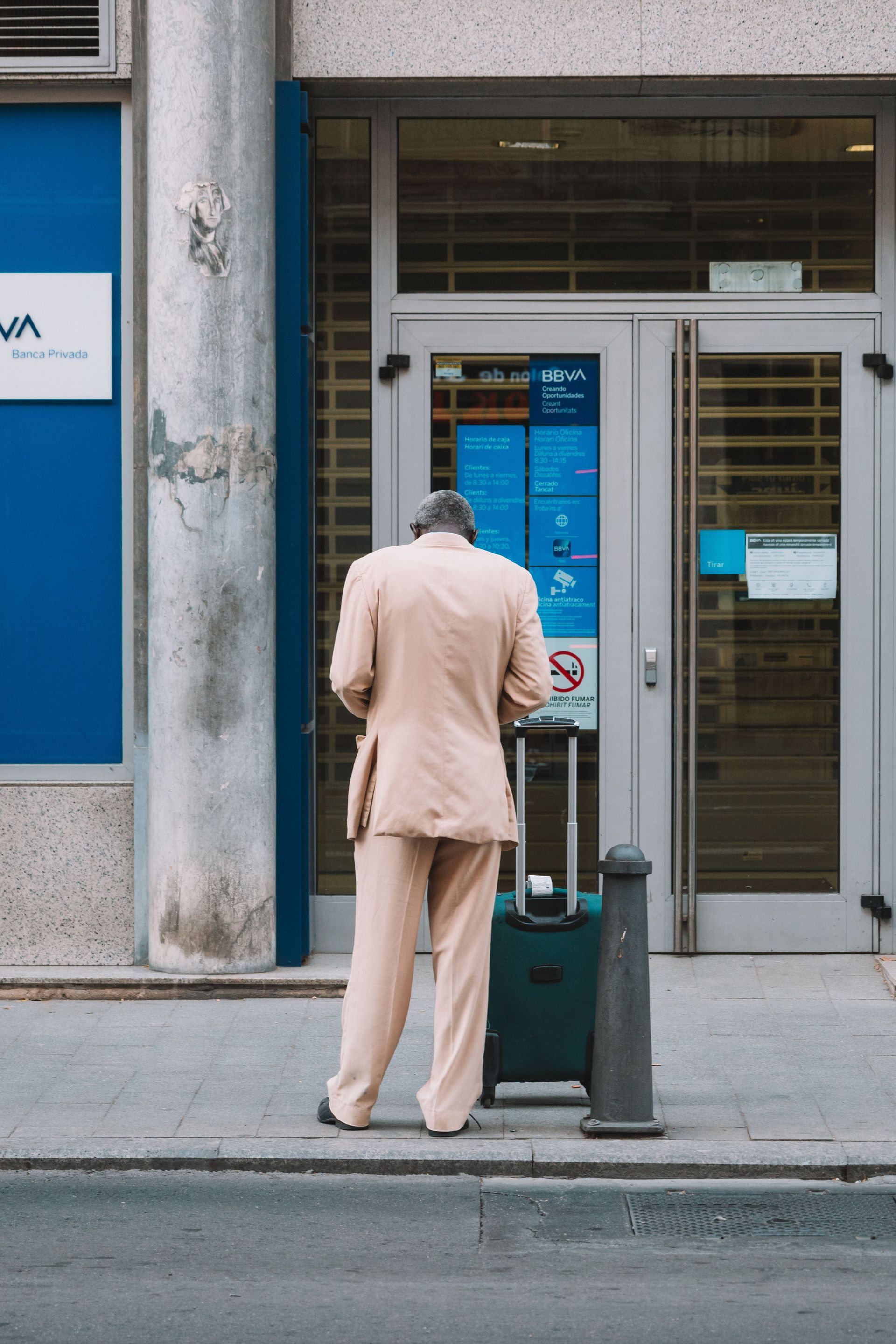 Person in a beige suit using a public payment kiosk outside a building.