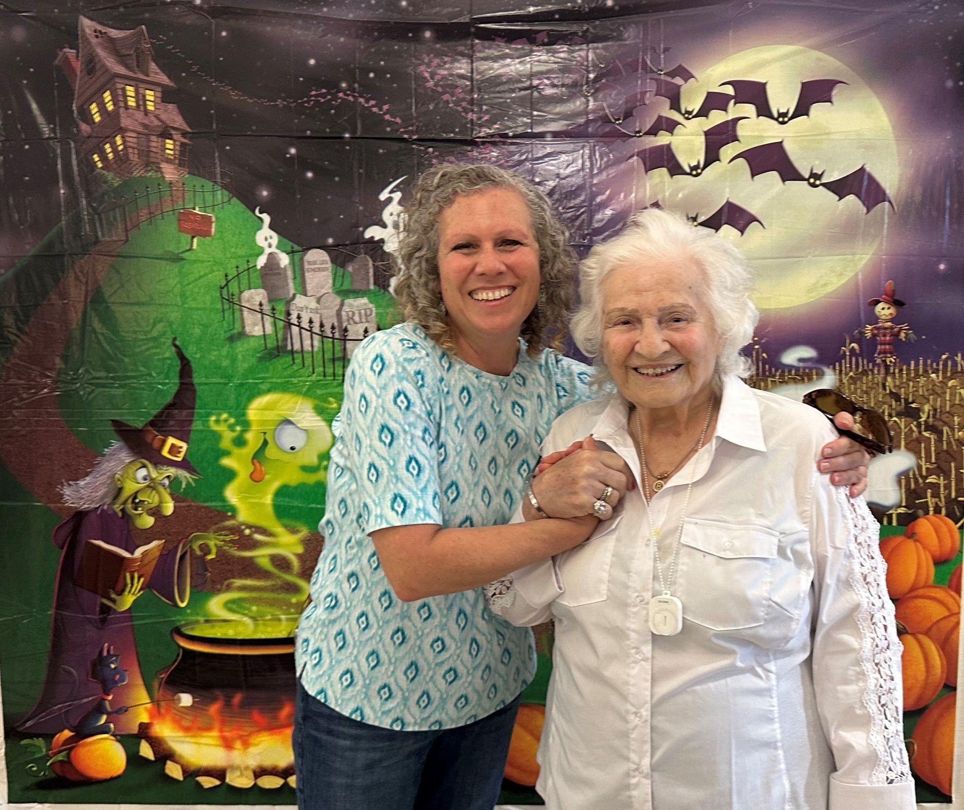 Two women are posing for a picture in front of a halloween backdrop.