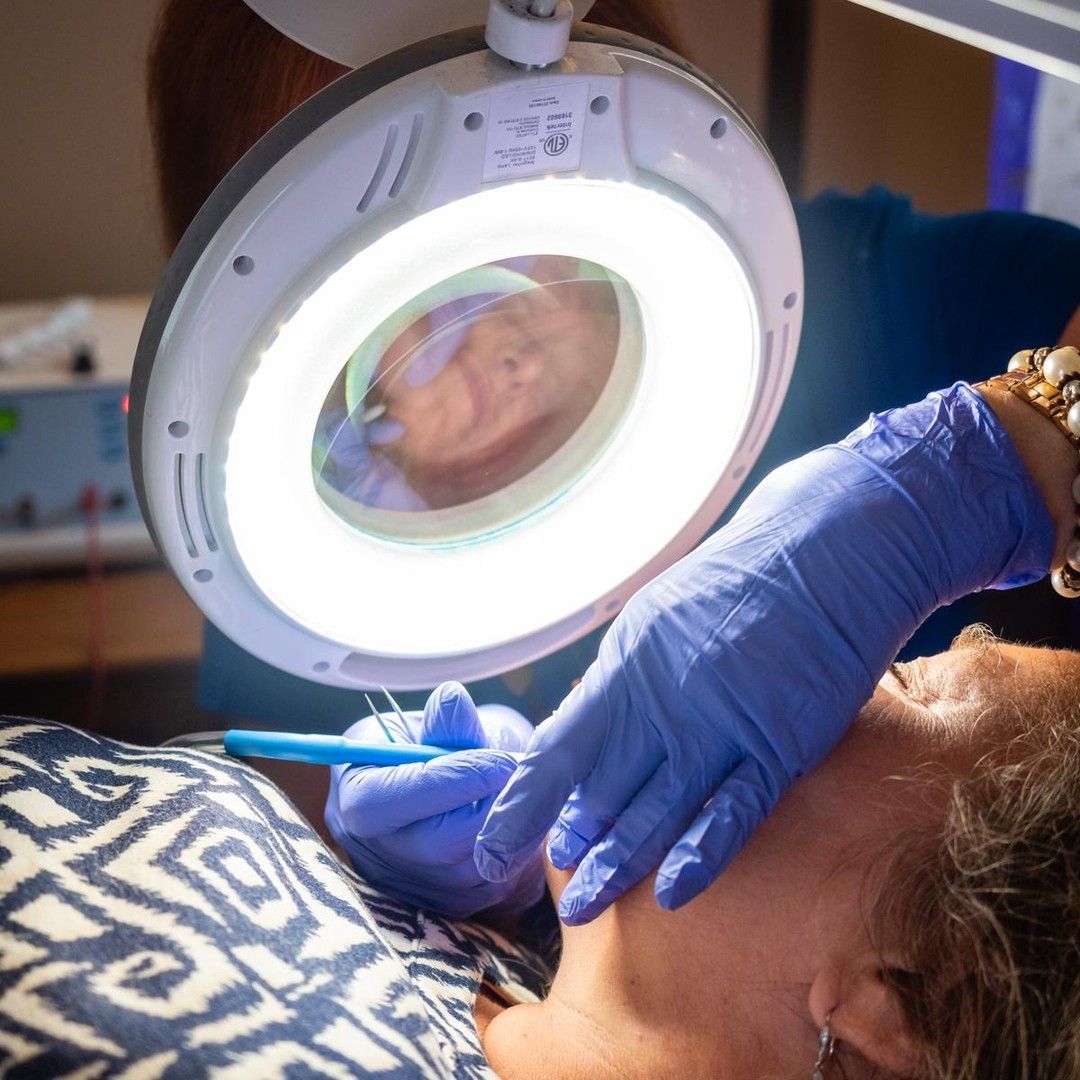Gloved clinician examining a patient’s face with a magnifying lamp during a skin treatment
