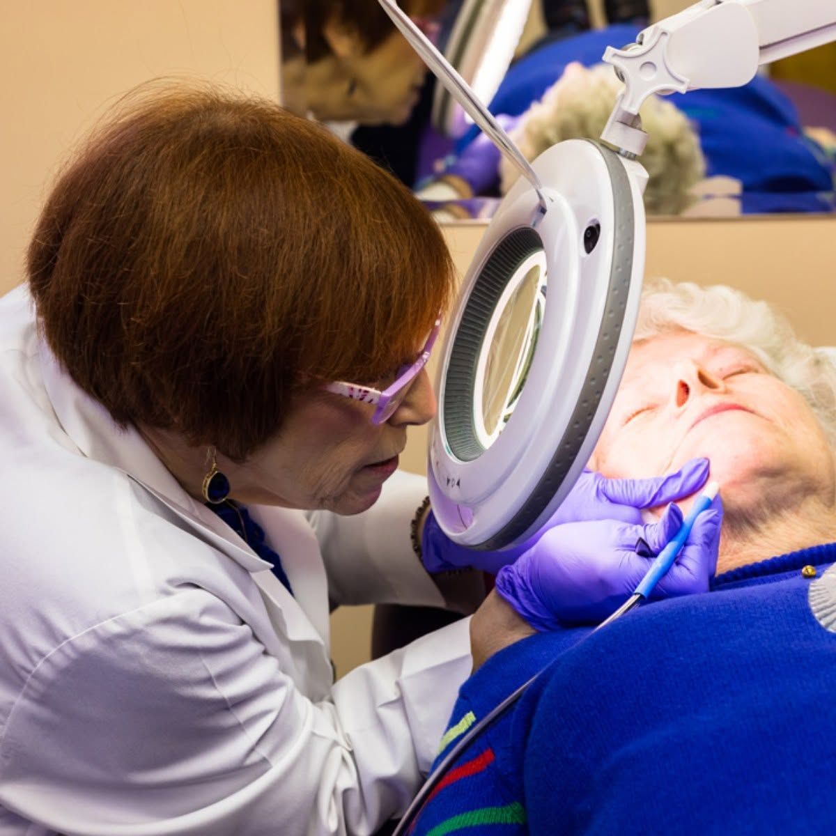 Healthcare worker examining a patient’s face with a magnifying lamp during a procedure