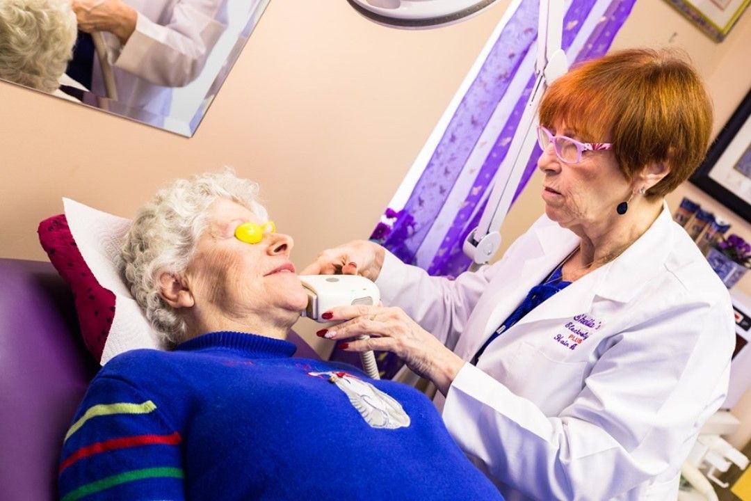 Caregiver tending to a reclining patient in a clinic, with the patient wearing a blue sweater and eye pad.