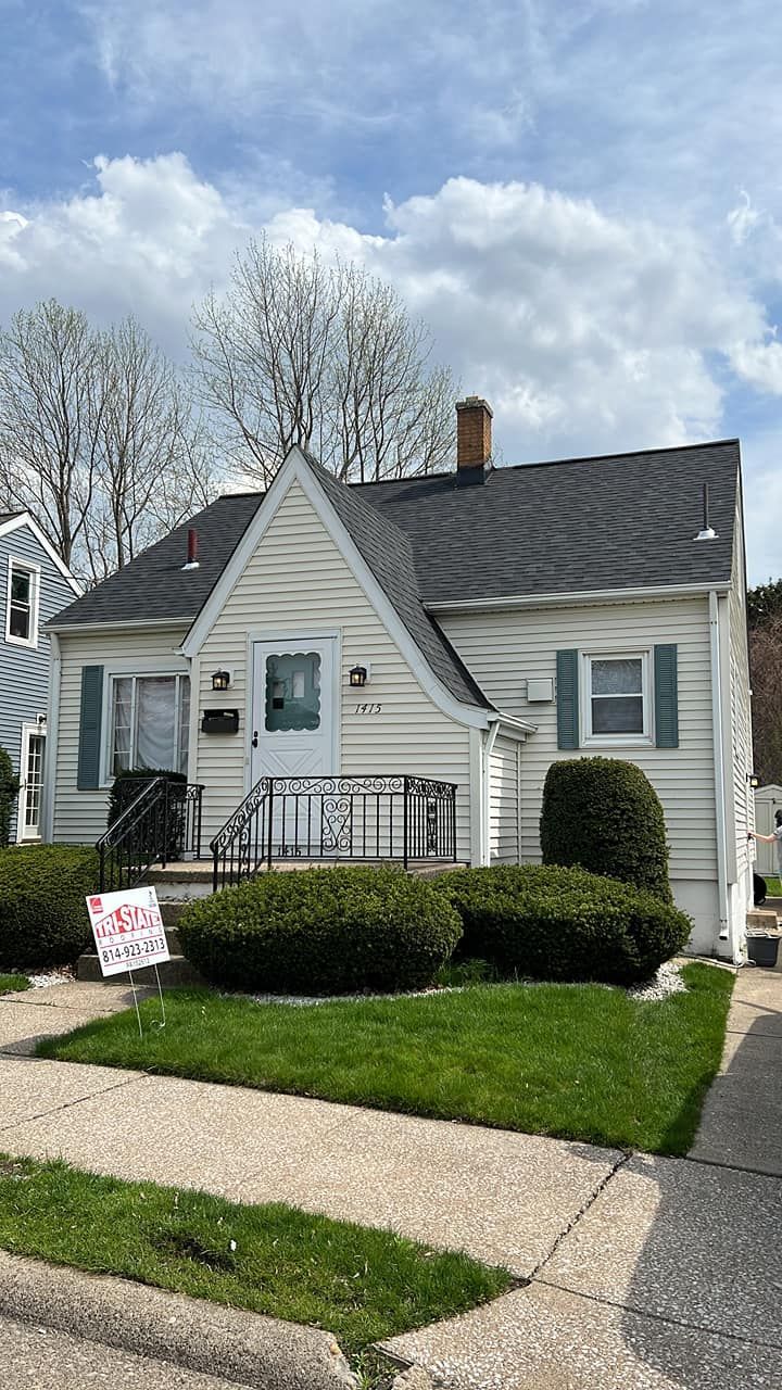 White house with a dark roof, green lawn, and shrubs, on a sunny day.