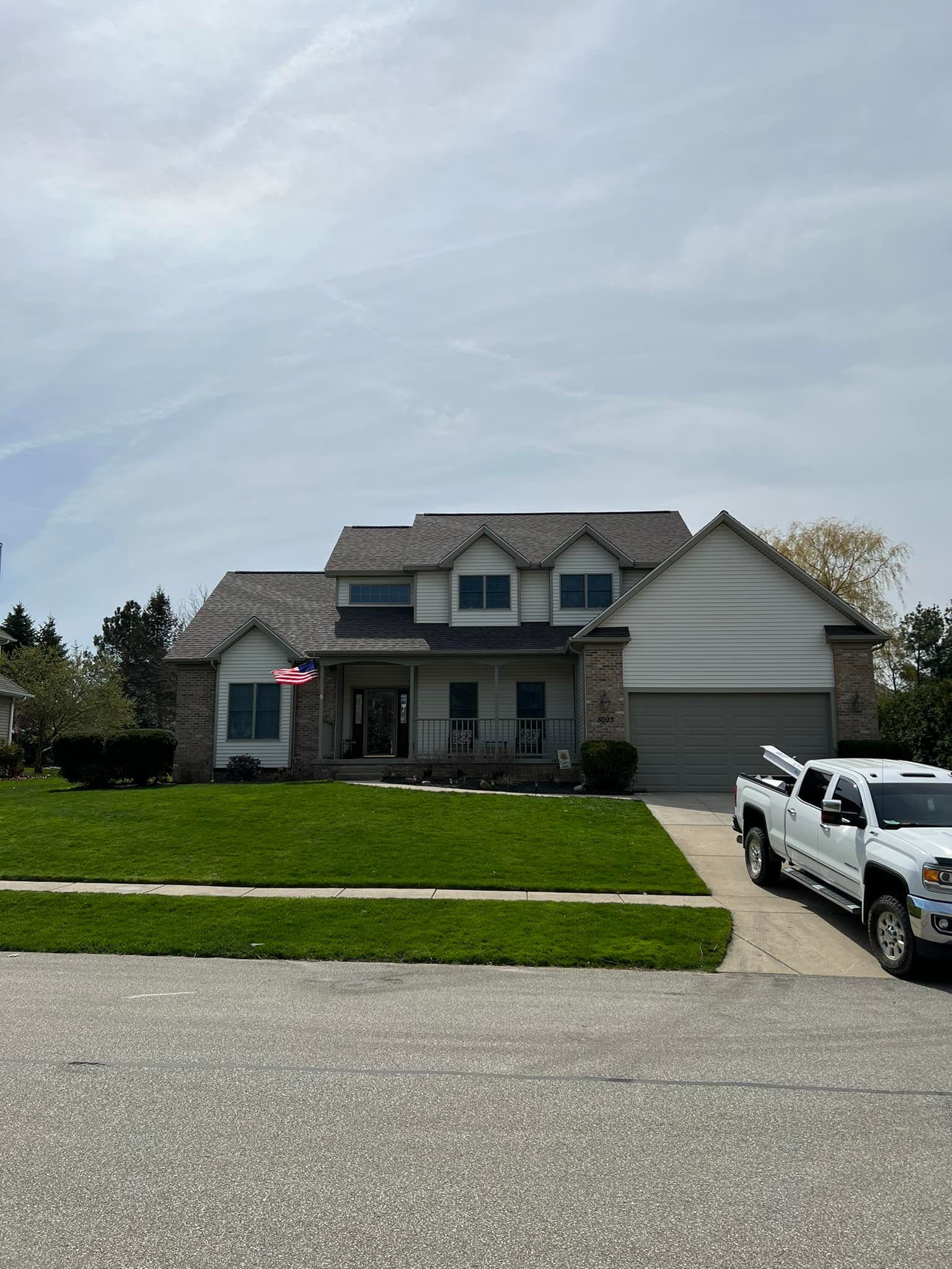 House with brick and white siding, green lawn, white truck parked in driveway.