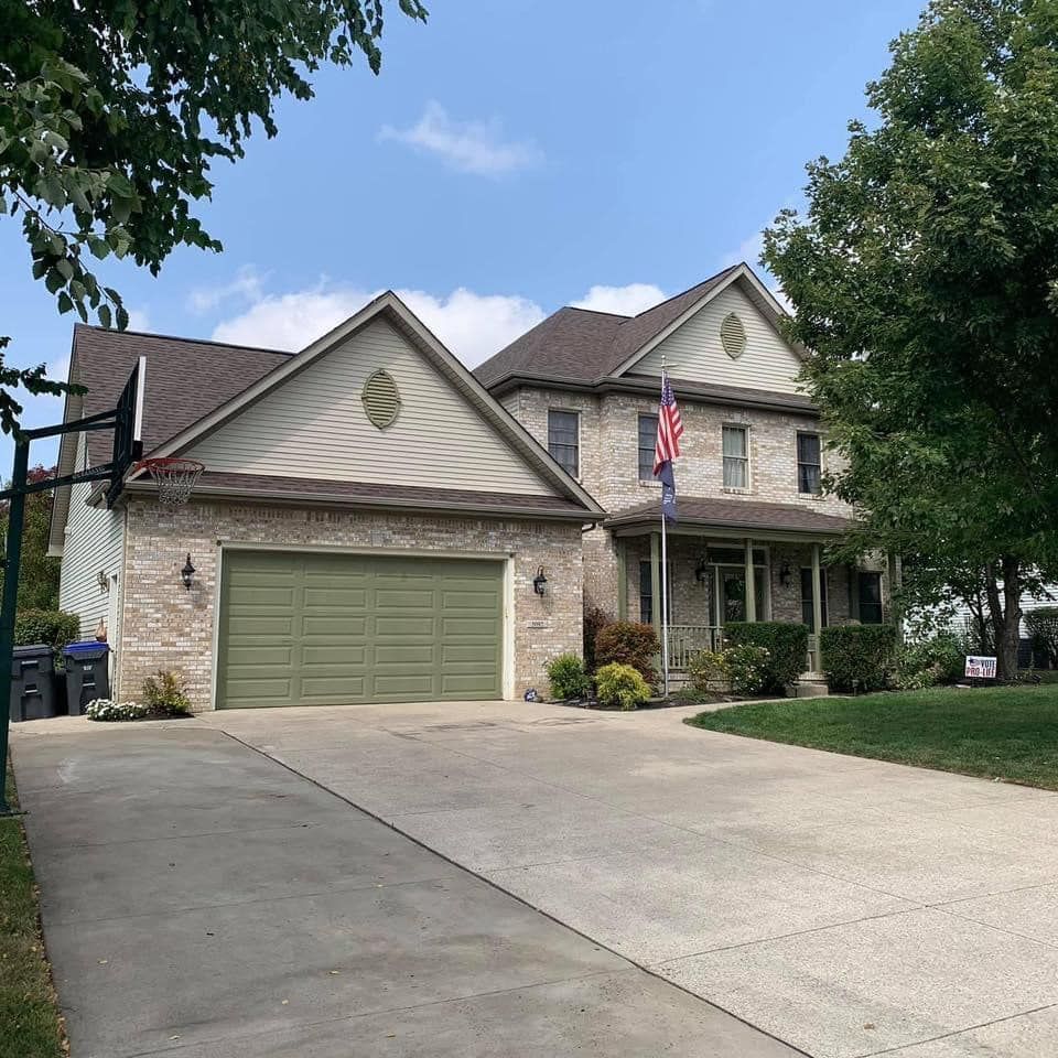 Two-story house with a brick facade and a green garage door, a driveway, and a basketball hoop.