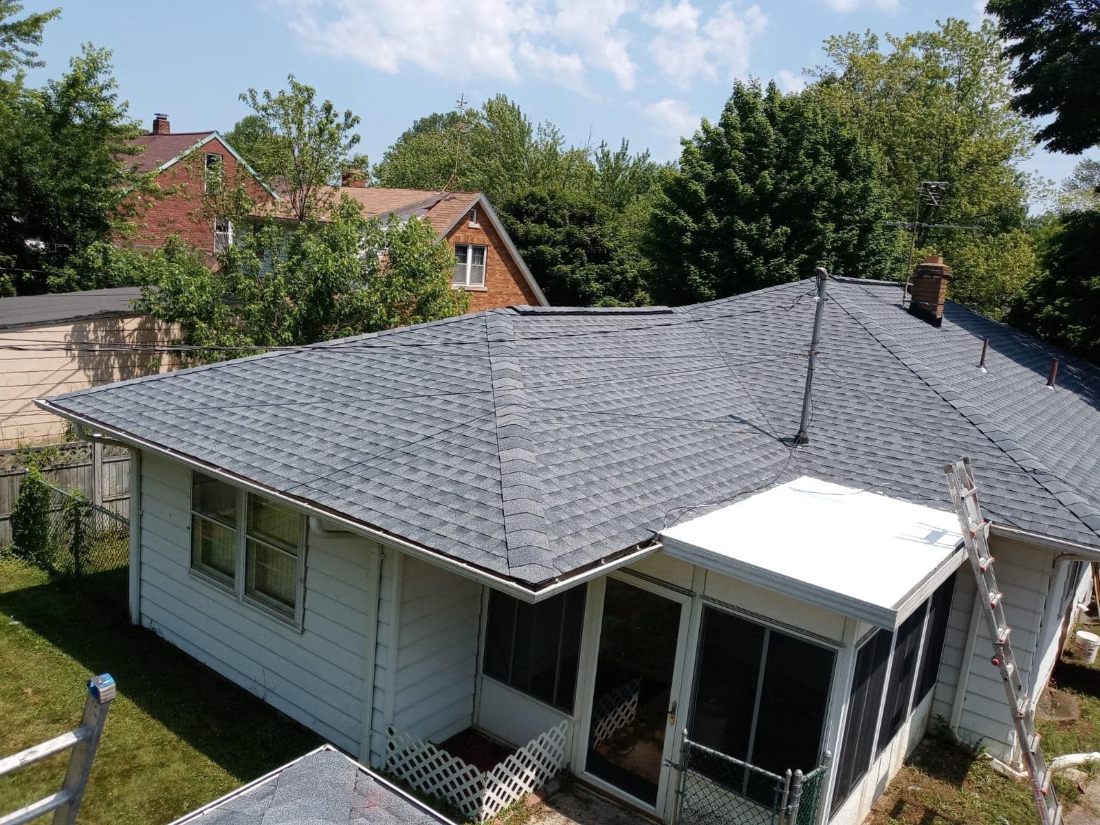 View of a house with a newly shingled roof and attached screened-in porch, under a sunny sky.