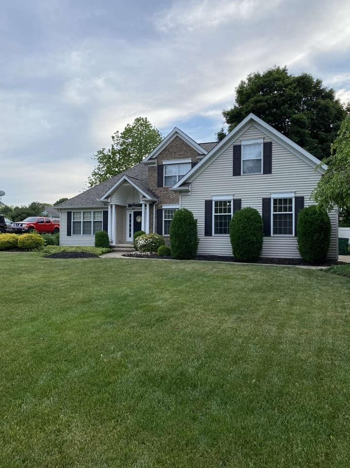 House with light siding, black shutters, and green lawn. Cloudy sky in the background.