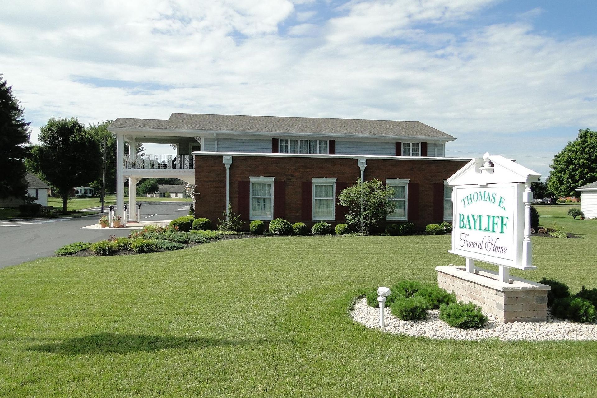 A building with a sign that reads "Sunrise Baycliff Senior Care Clinic" on a green lawn under a partly cloudy sky.