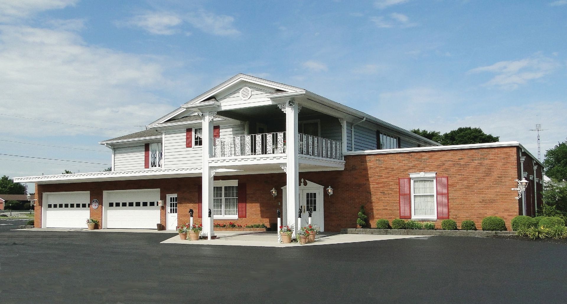 Two-story building with white balcony and garage, brick and white exterior, blue sky background.