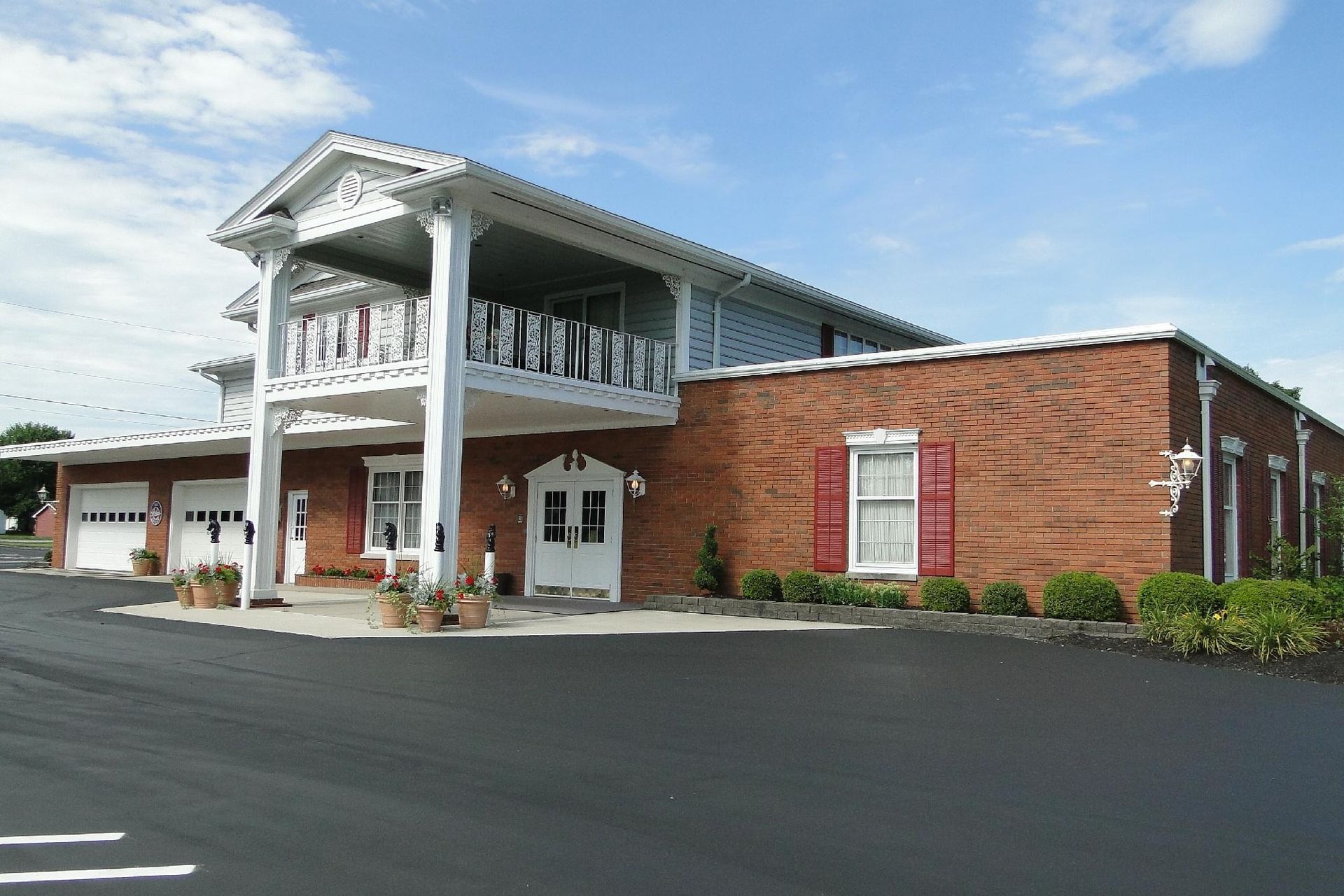 Building with two-story porch supported by white columns, red brick facade, and garage doors.