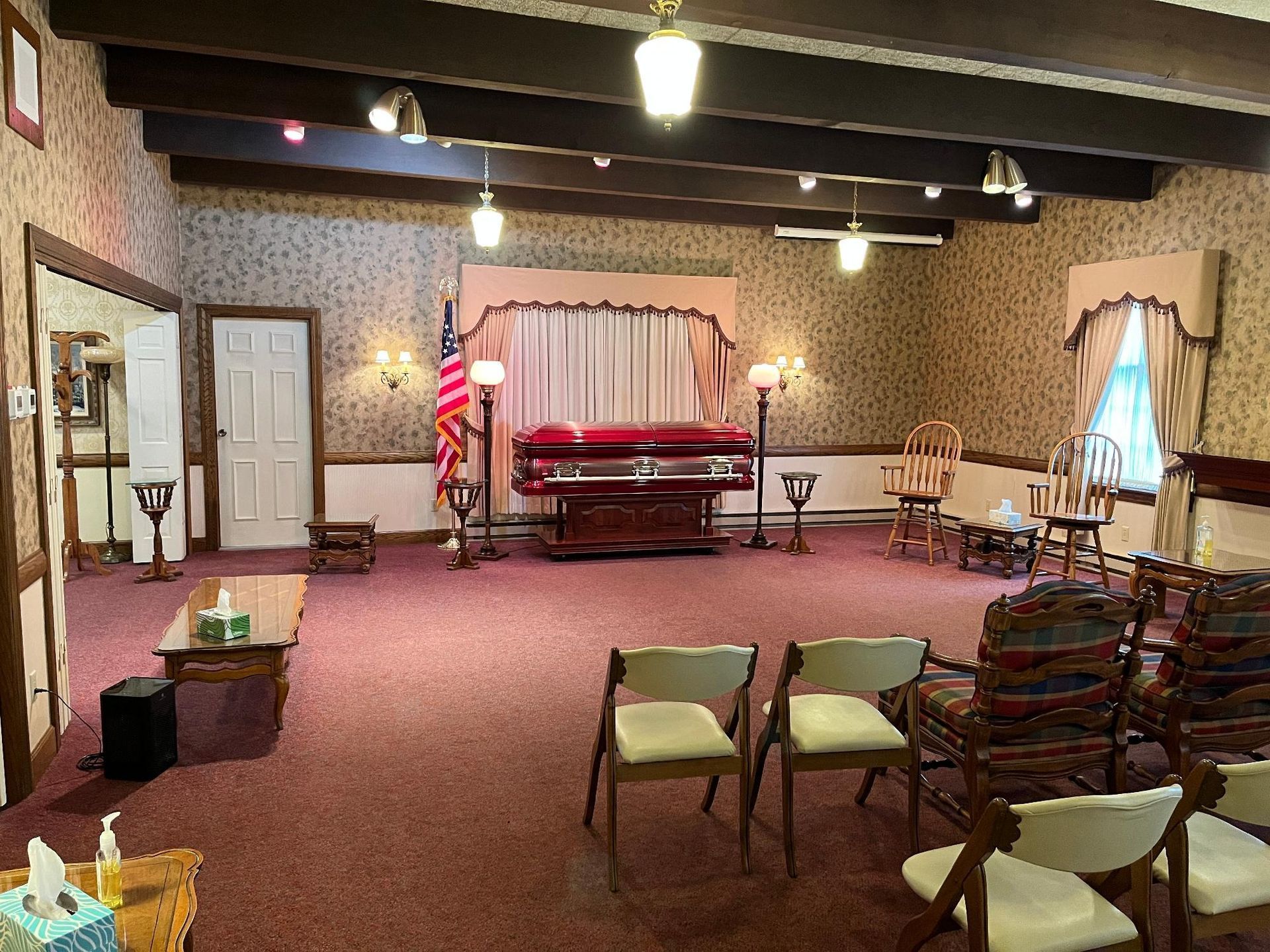 Funeral home interior with casket and chairs. Red carpet, beige walls, and wood accents.