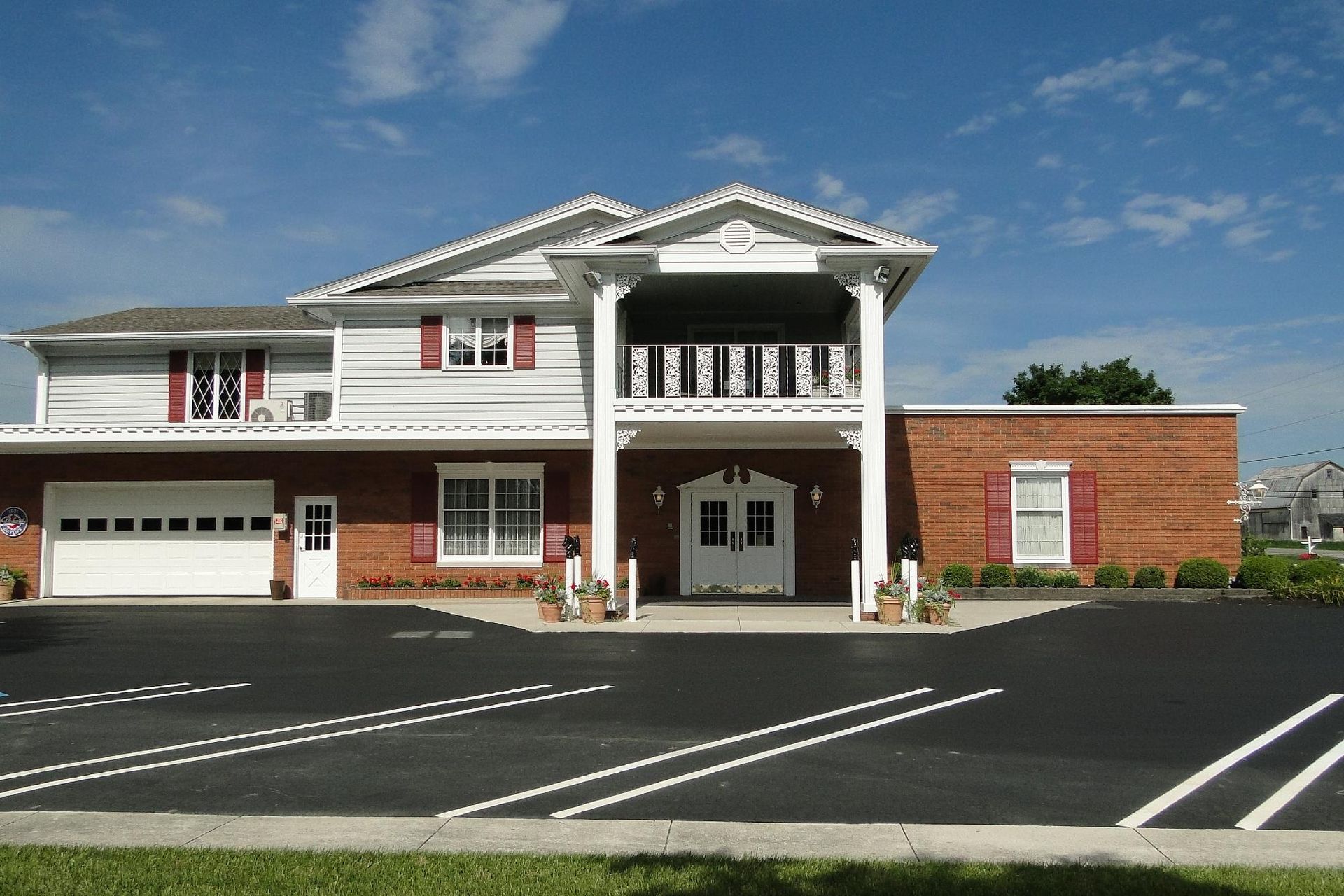 Two-story brick building with white pillars and a parking lot on a sunny day.