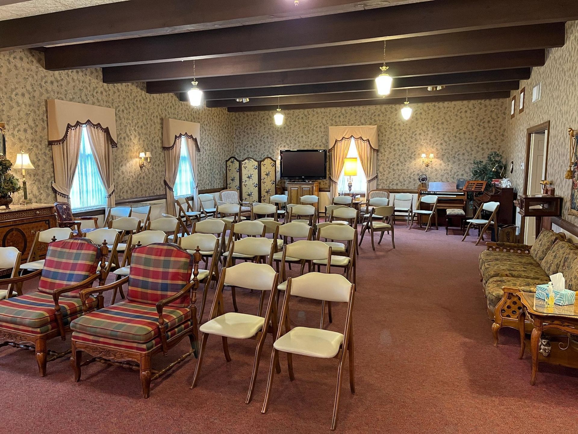 An empty room with rows of chairs, a large screen, and floral wallpaper.