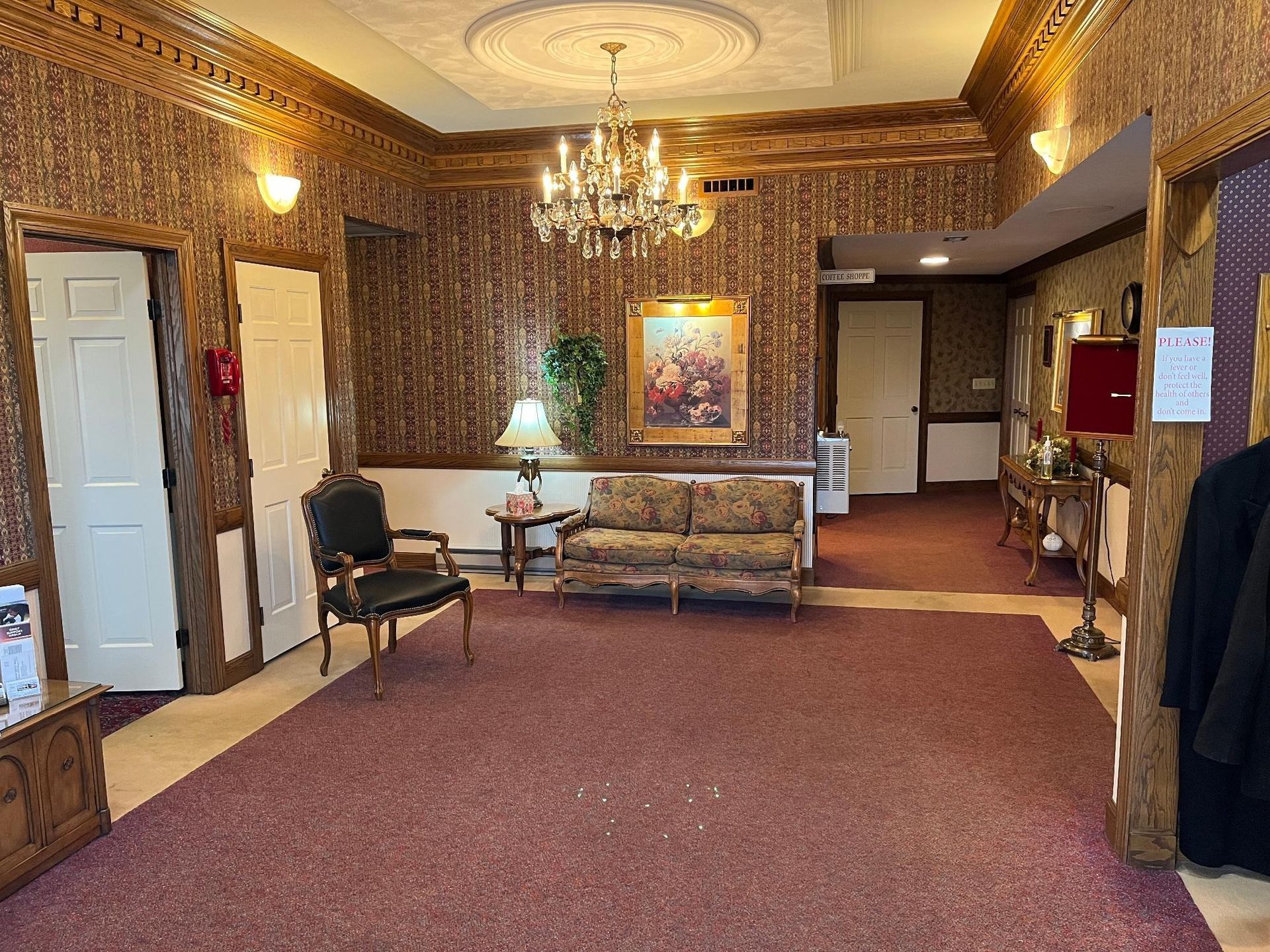 Lobby with patterned walls, red carpet, chandelier, sofa, art, and doors.