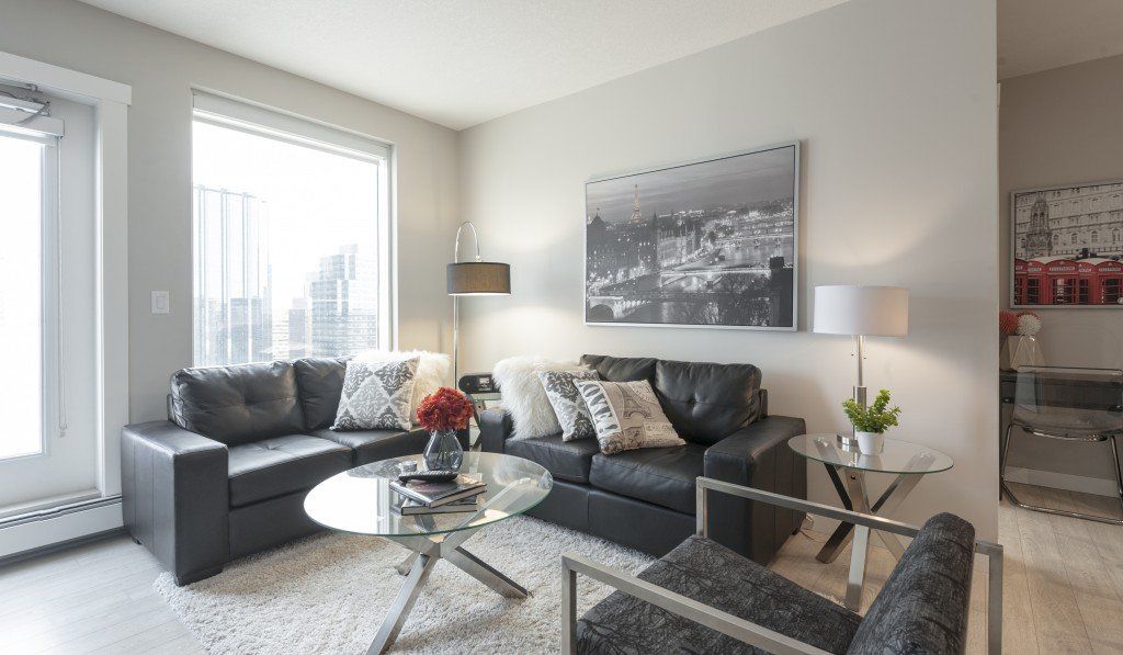 Living room with black leather sofas, glass coffee table, white rug, and city view. Edmonton executive Suites