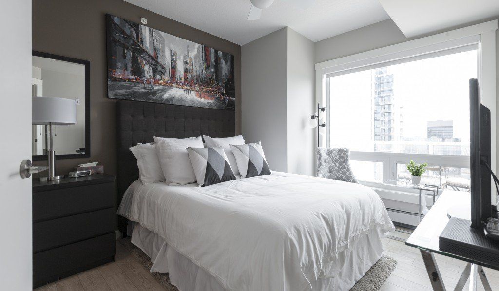 Bedroom with white bed, dark gray headboard, artwork, and large window.