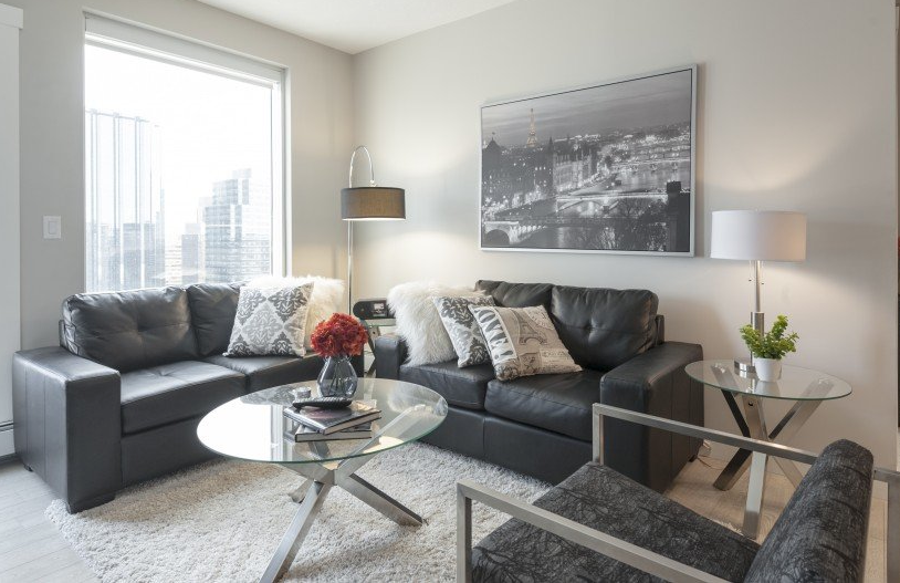 Living room with gray leather couches, glass coffee table, and cityscape art.