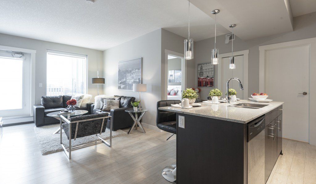 Modern open-concept living space with kitchen island, living room with black furniture, and large windows.