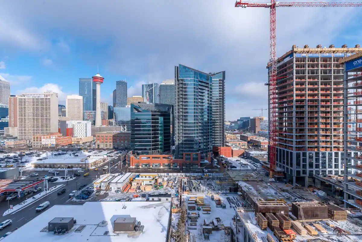 City skyline with construction. Snow covers the foreground. Blue sky with a red crane. Calgary furnished suites 