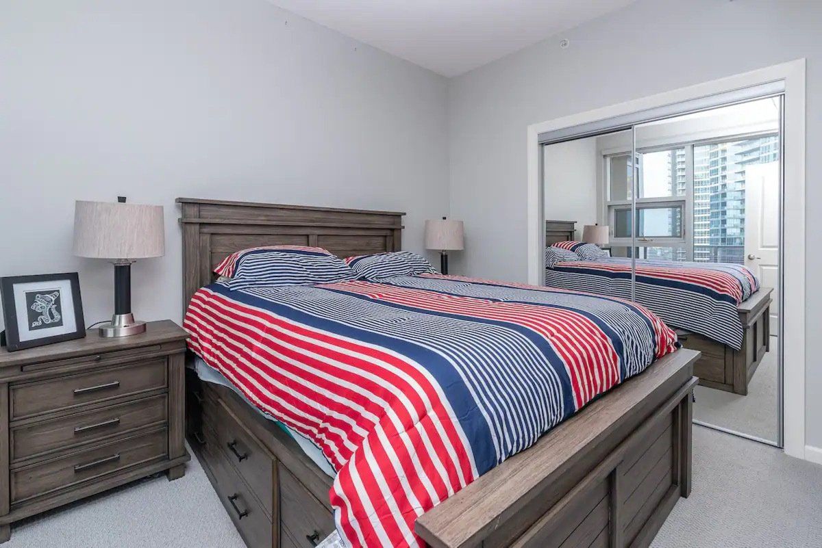 Bedroom with a wooden bed, nightstand, and a closet with mirrored doors. The bed has red and blue striped bedding.