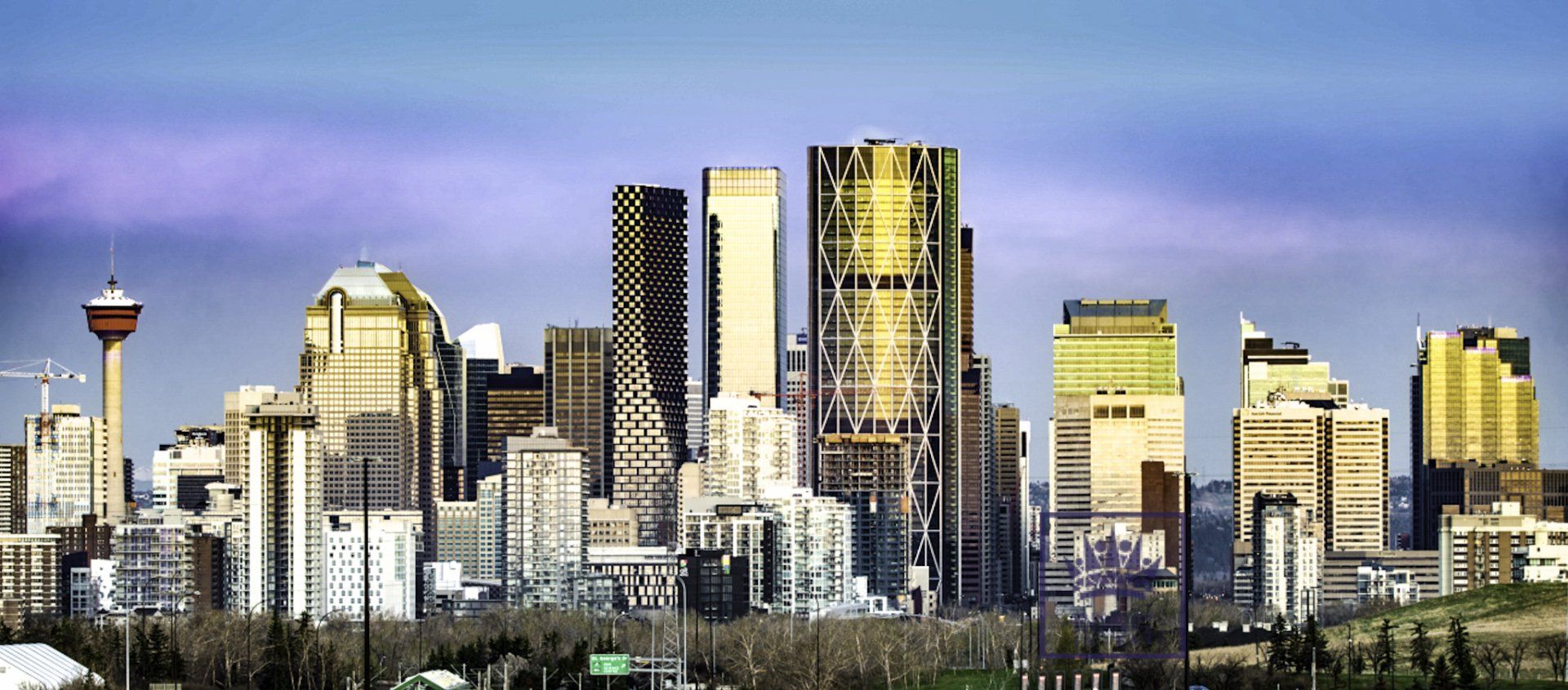Skyline of Calgary, Alberta, Canada; featuring skyscrapers and the Calgary Tower under a blue sky.