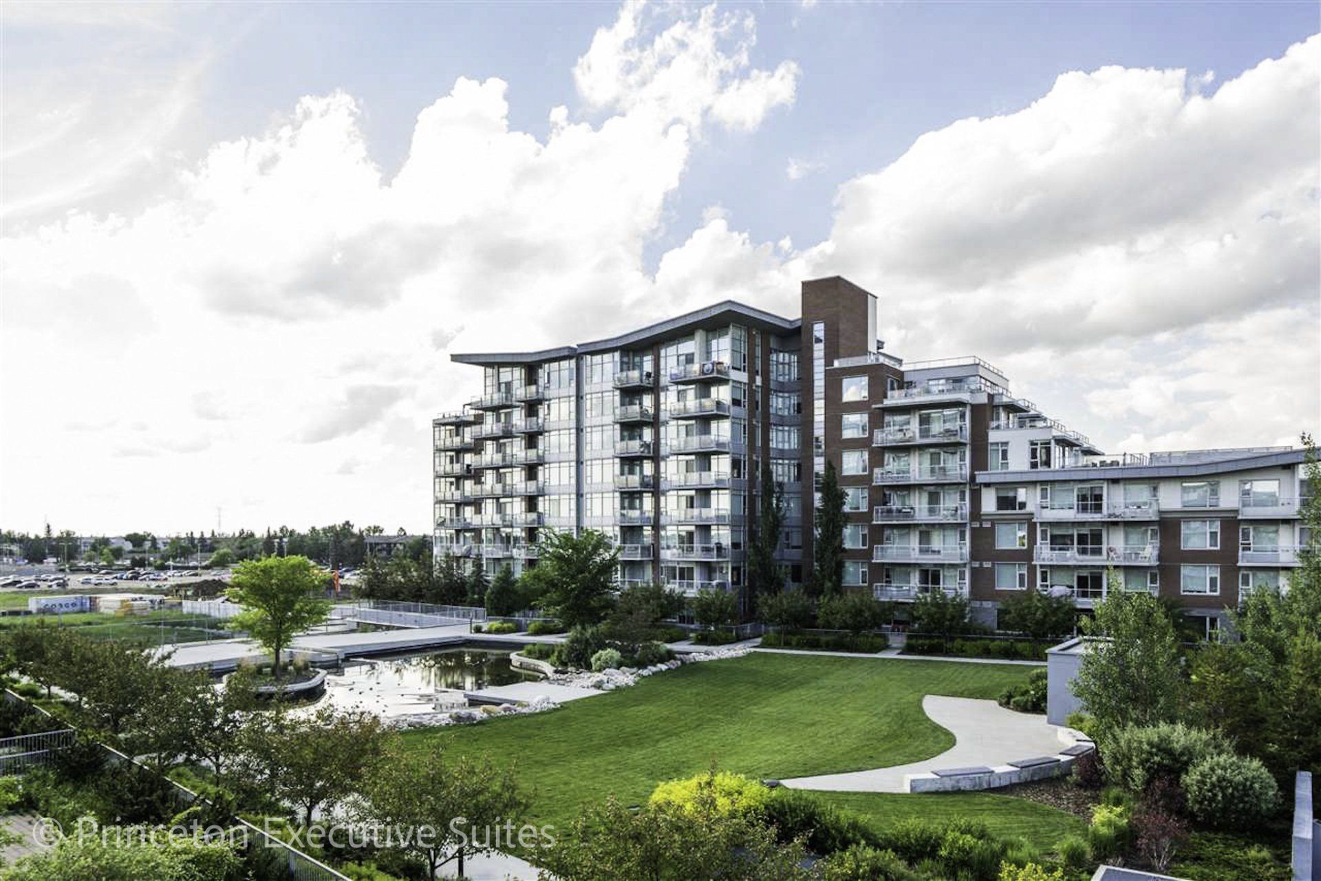 8 Storey building that has a large freeway and pond in front of it on a sunny day