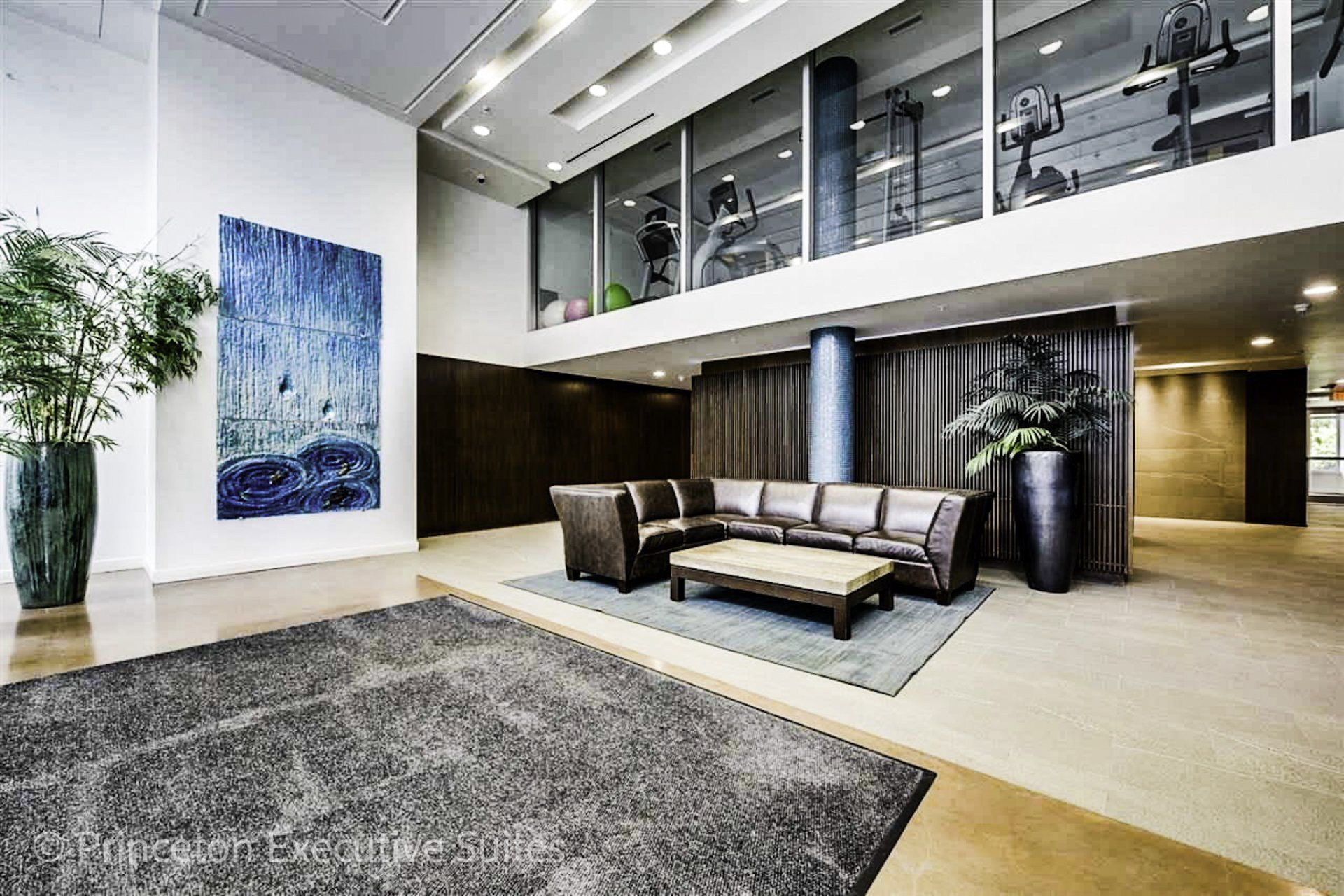 Large marble lobby area stunningly decorated with giant plants and modern blue abstract artwork. Large brown sectional couch.