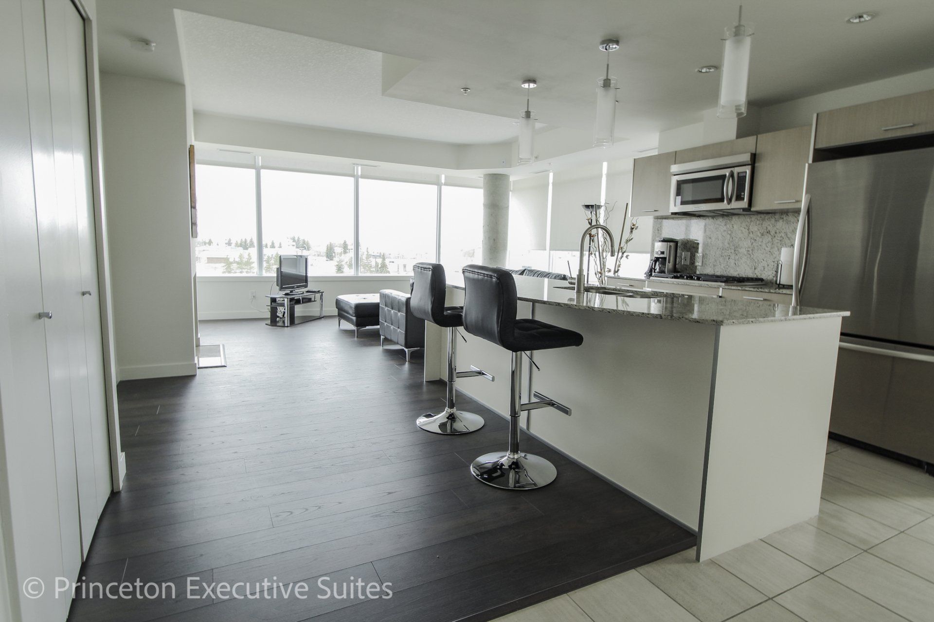 Modern kitchen with bar stools, large windows, and dark wood floors.