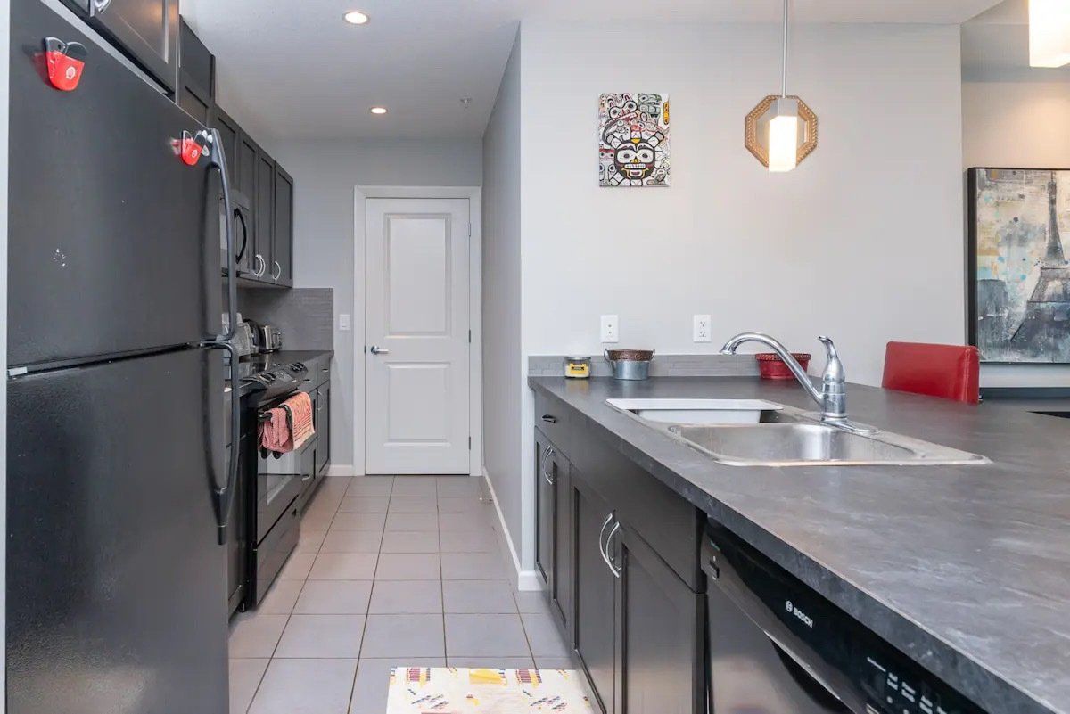 Modern kitchen with black appliances, gray countertops, and a doorway in the back.