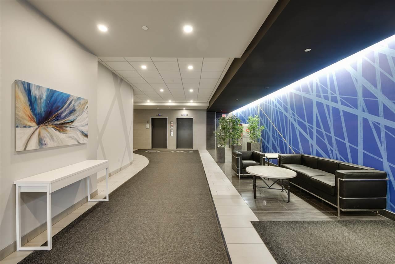 Lobby with blue accent wall, seating area, artwork, elevators. Long hallway with gray carpet, white table.