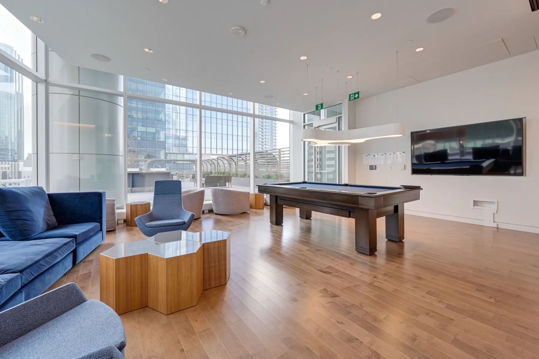 Spacious modern lounge with a pool table, blue sofas, and large windows overlooking a city.