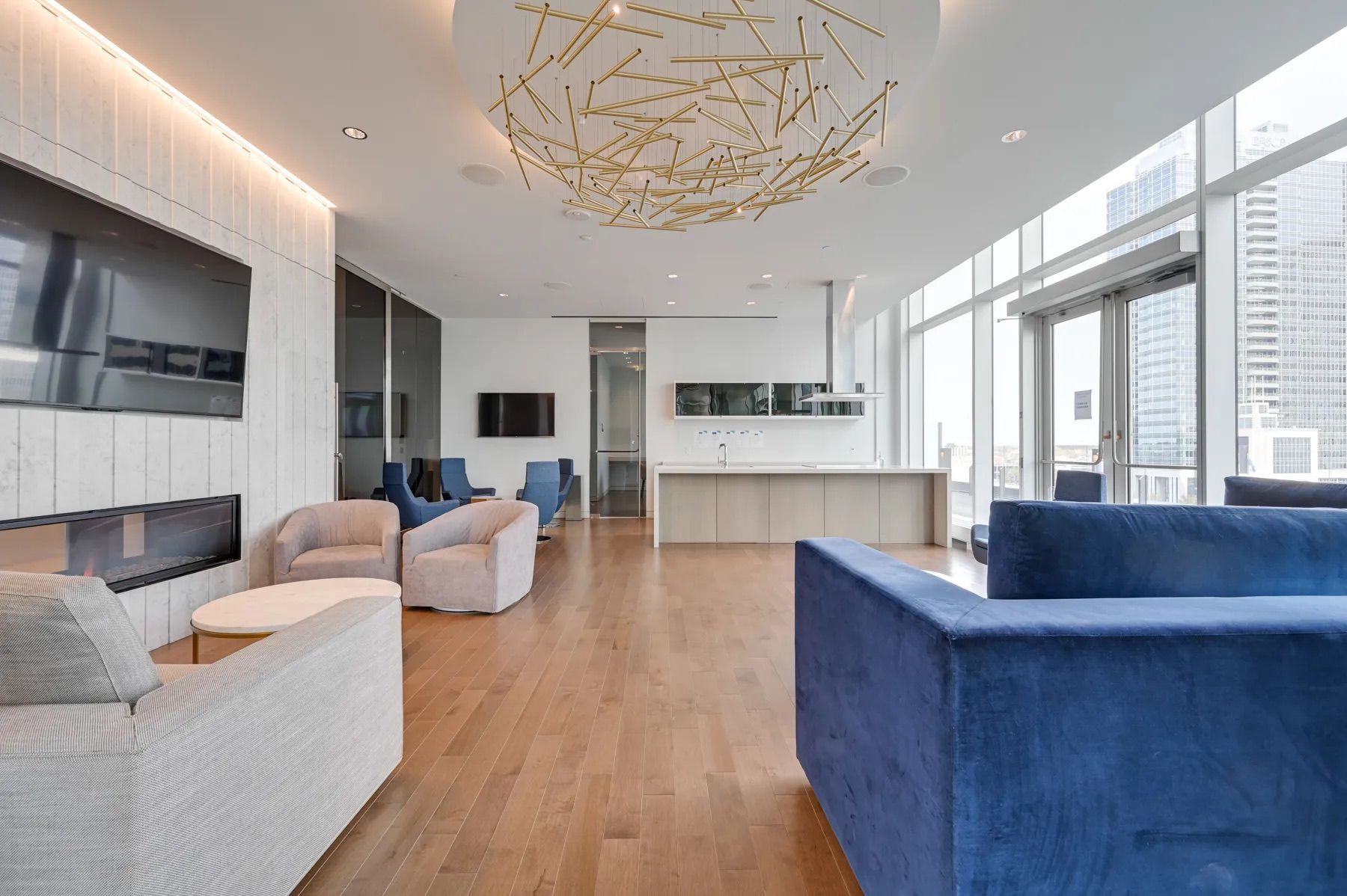 Modern lounge with blue and beige furniture, fireplace, kitchen, and city view.