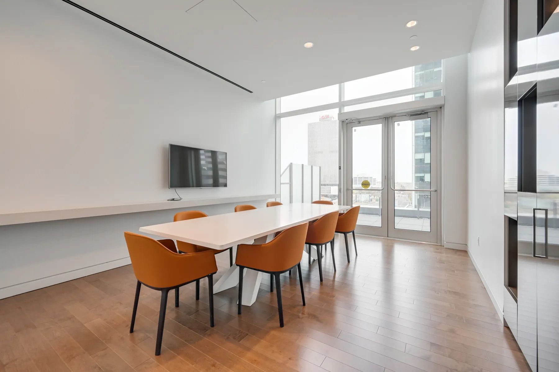 Modern conference room with orange chairs around a white table, near a glass door.