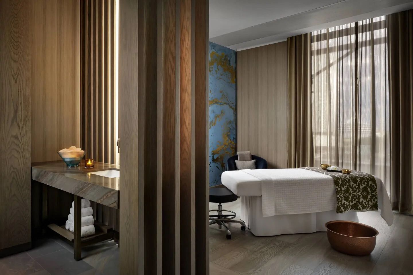 Spa room: massage table, sink, and decorative wooden panels. Neutral colors with a blue accent wall.