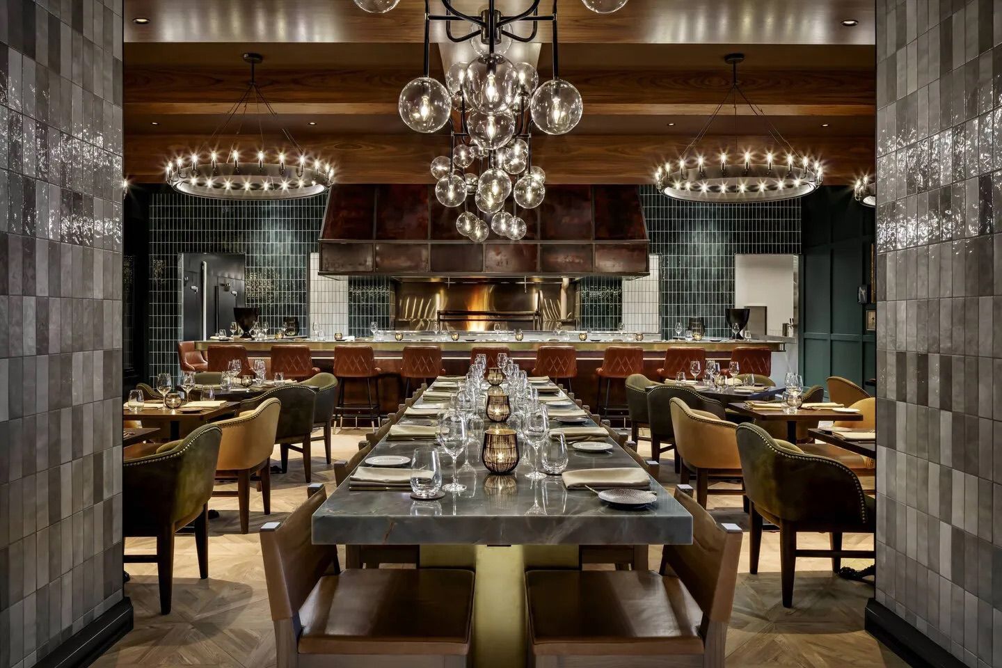 Upscale restaurant interior. Long table set for dining, other tables around it. Dark decor, lighting.