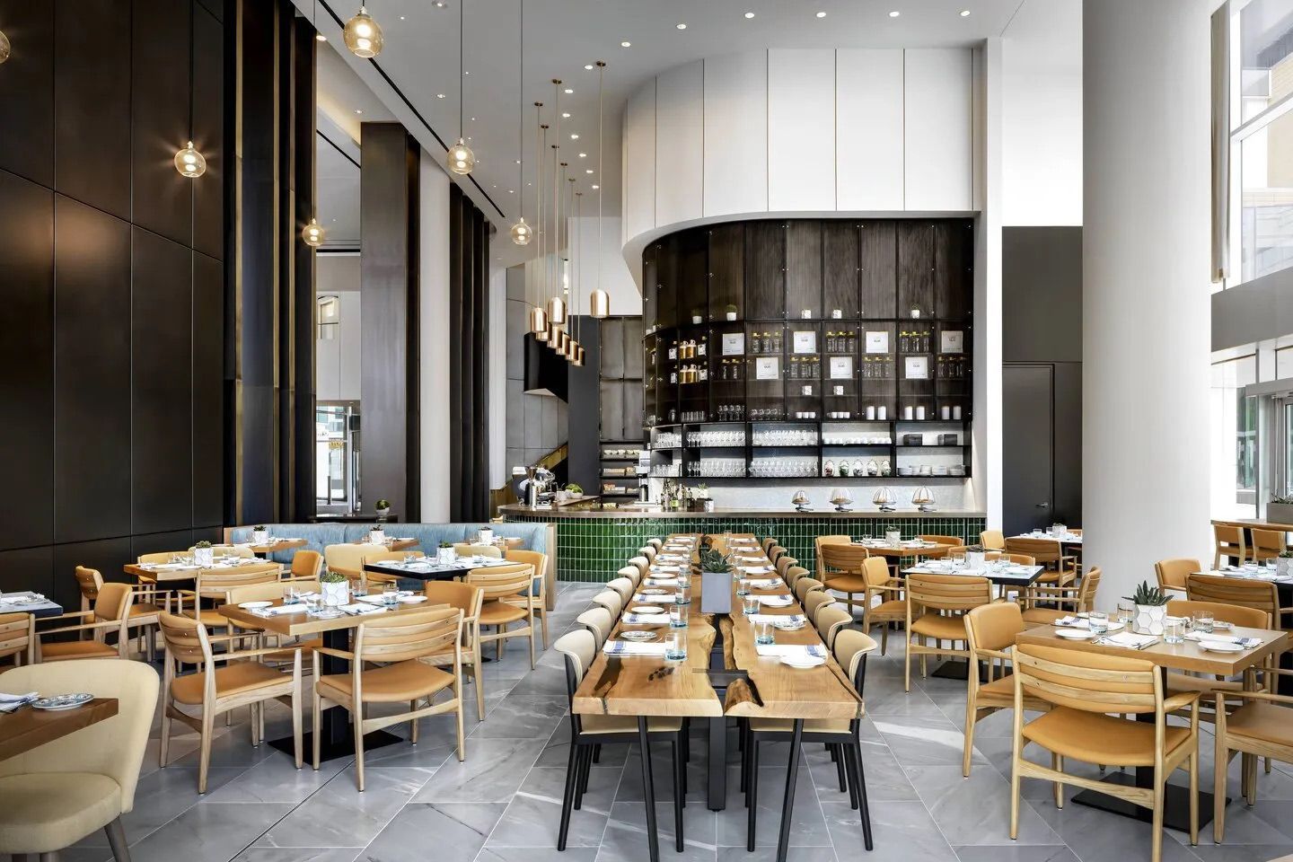 Modern restaurant interior with wooden tables and chairs, marble floors, and a green bar.