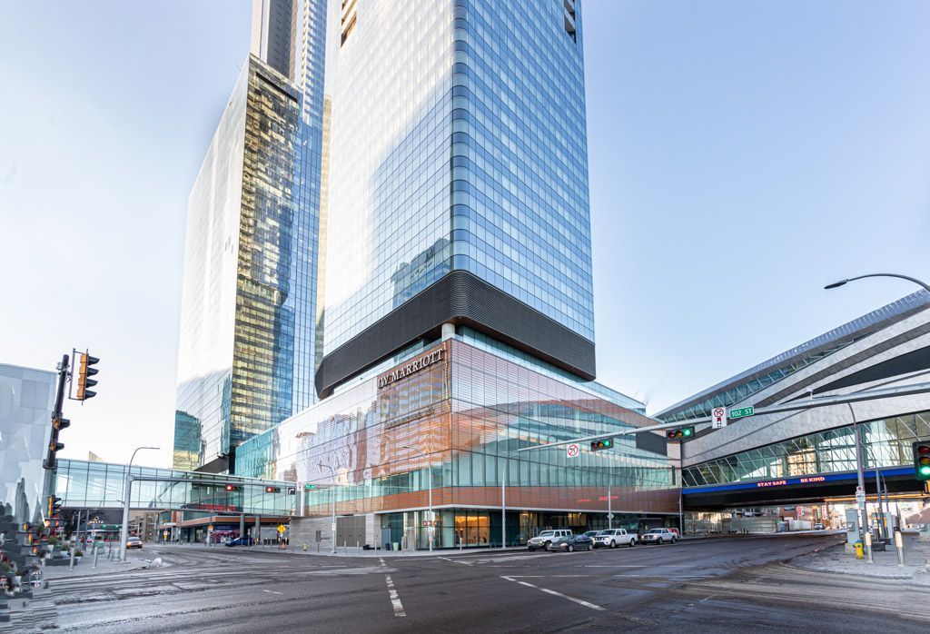 Modern skyscraper with glass facade, brown base, and pedestrian bridge, in an urban setting.