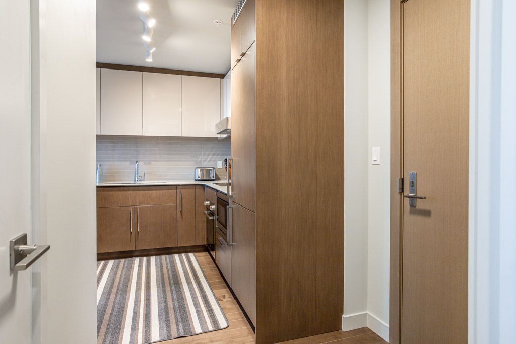 Hallway with wooden cabinets, leading to a kitchen with a striped rug and oven.