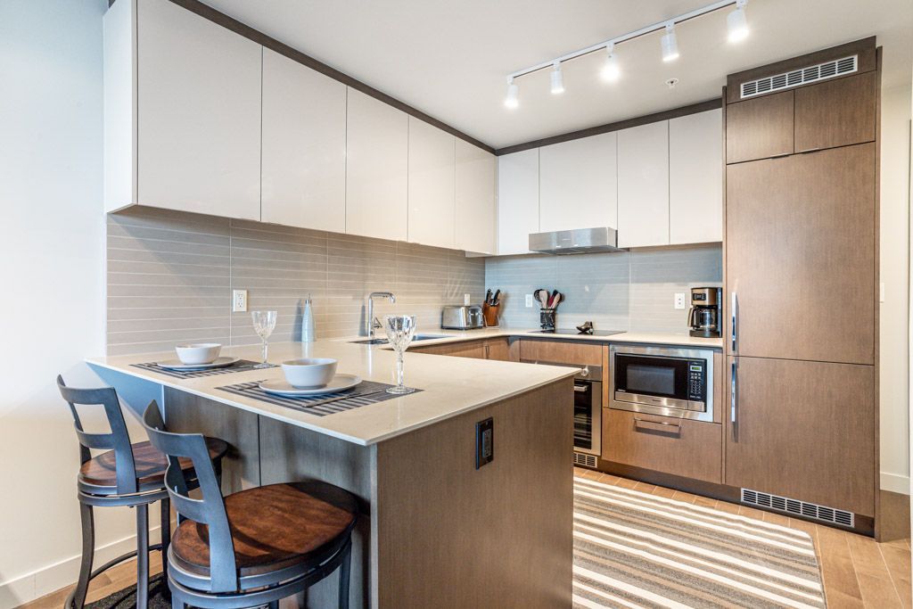 Modern kitchen with island and bar stools, featuring white cabinets and stainless steel appliances.