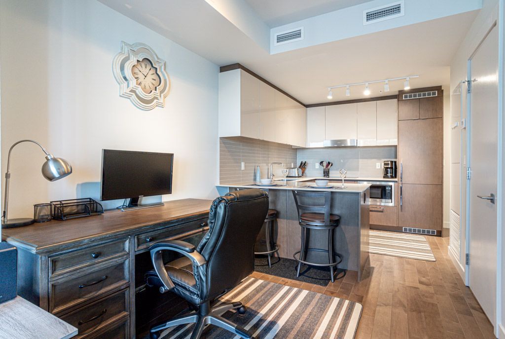 A modern office space with a desk, kitchen, and dark wood flooring.