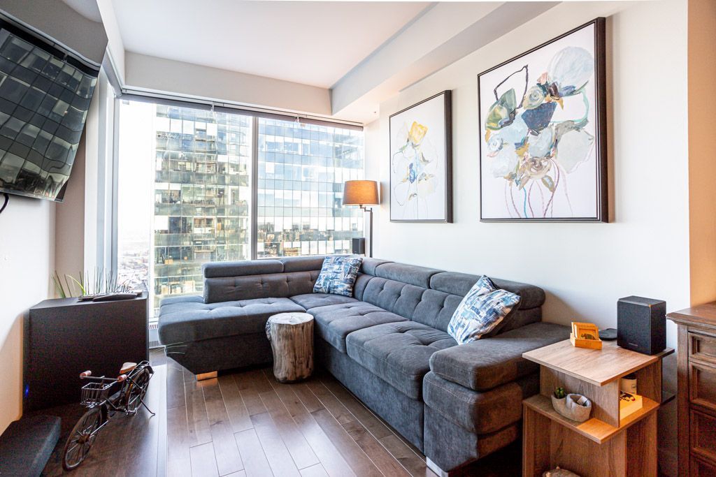 A modern living room with gray sectional sofa, artwork, and city views.