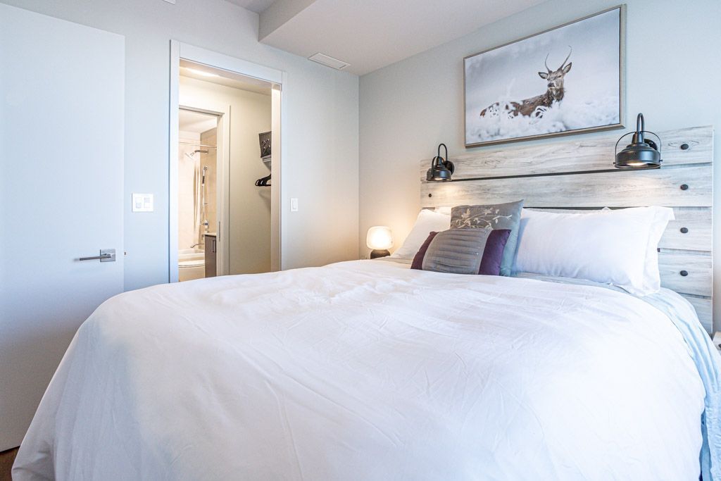 Bedroom with white bedding, wooden headboard, art of an elk, and a view of a bathroom.