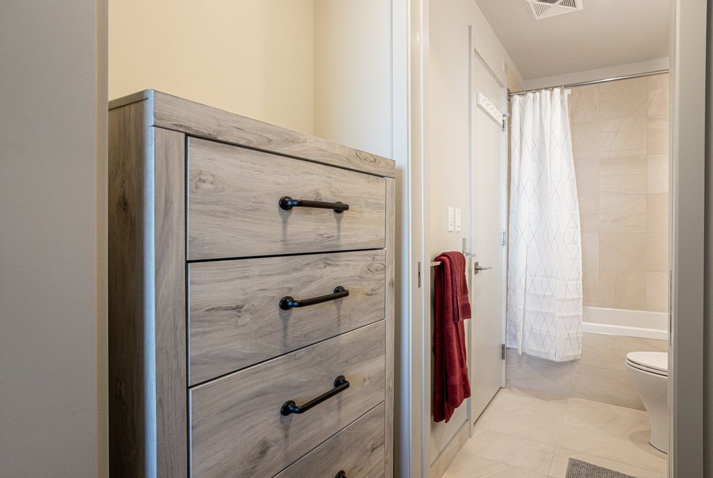 A light-colored dresser in a hallway, next to a bathroom with a shower curtain.
