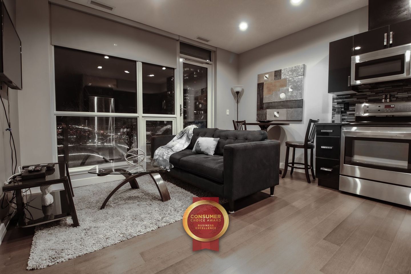 Large bedroom with grey bed and white linens on the bed daytime, Dark espresso coloured hardwood flooring
