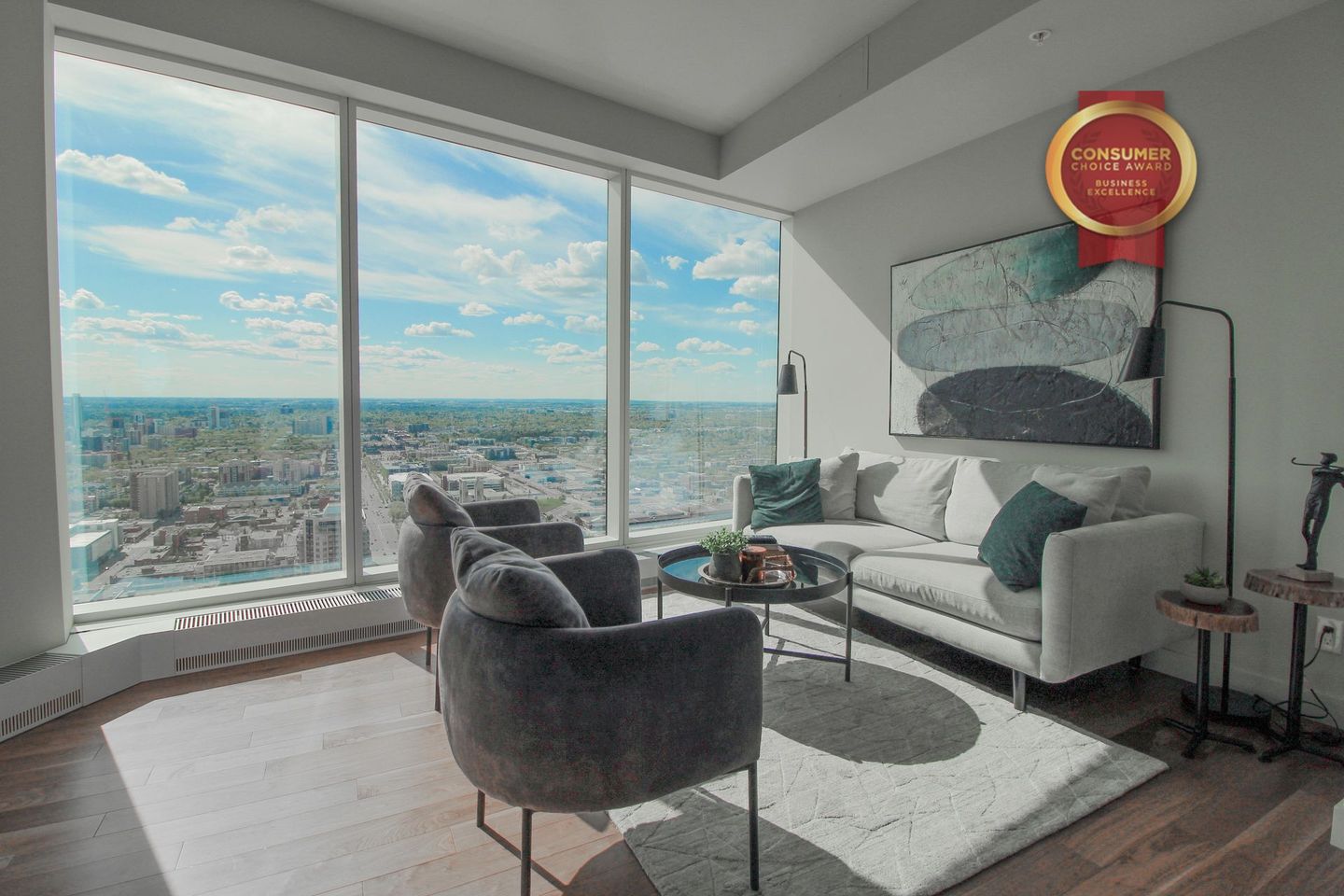 Furnished condo with ceiling to floor windows overlooking downtown Edmonton Grey couch and 2 chairs and a black round table